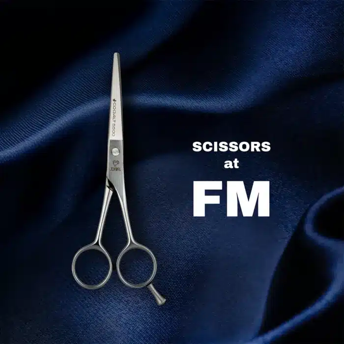 A pair of professional hairdressing scissors with a sleek design is placed on a dark blue satin fabric. Text beside the scissors reads SCISSORS at FM.