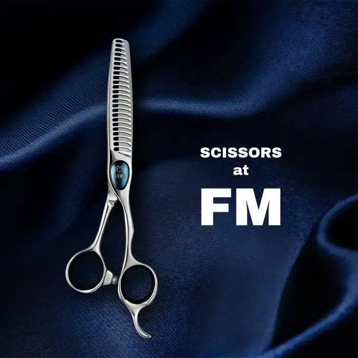 A pair of silver hair thinning scissors placed on a dark blue silky fabric. Text next to the scissors reads Scissors at FM. The backdrop adds a luxurious context to the professional styling tool.