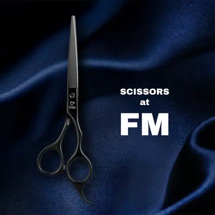 Black scissors on a dark blue fabric background. Text reads SCISSORS at FM in white, positioned to the right of the scissors.